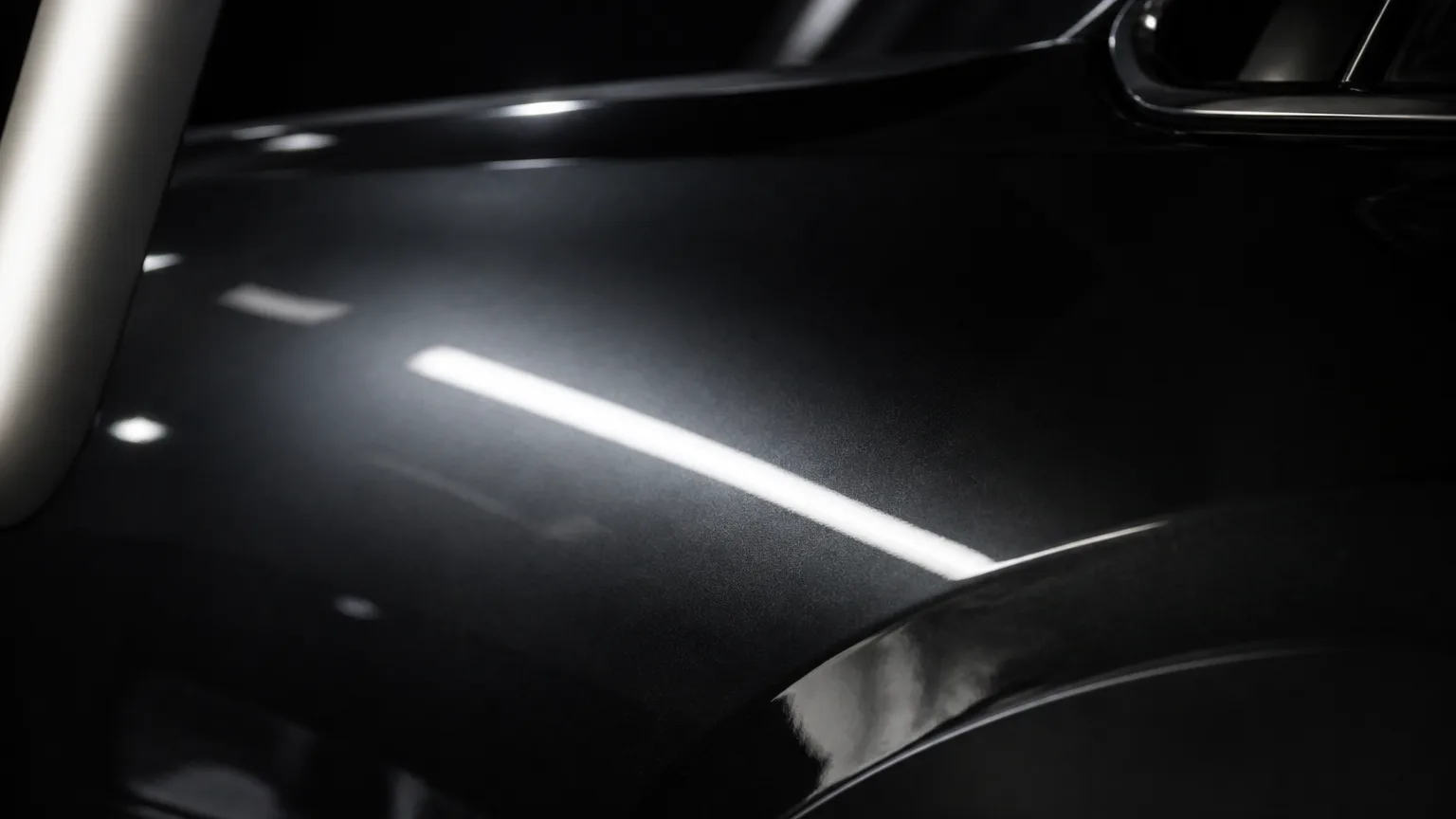 Glossy dark automotive paint under a linear inspection light.